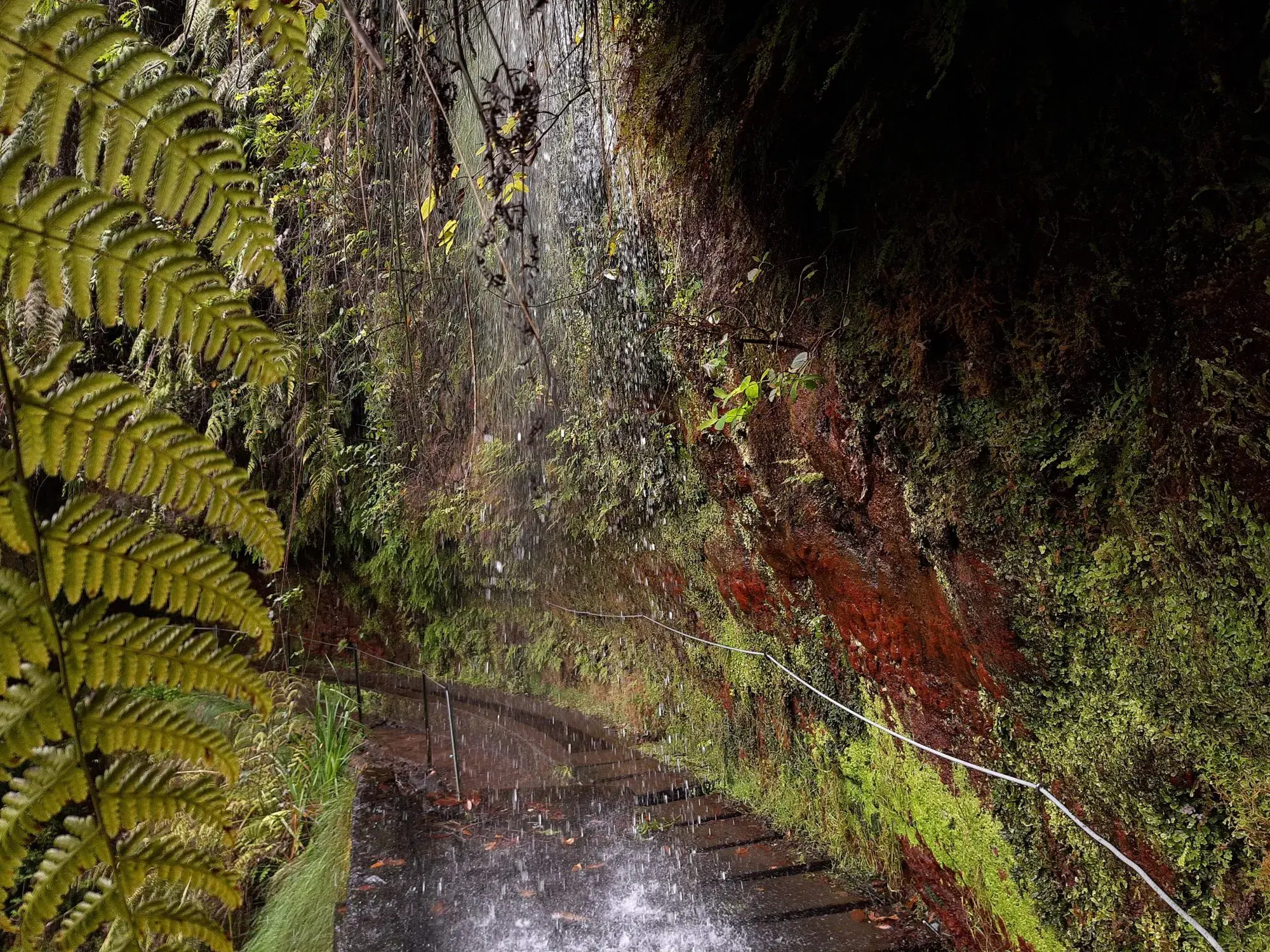 Waterfall pouring over the rock face onto the Levada do Rei path on PR 18